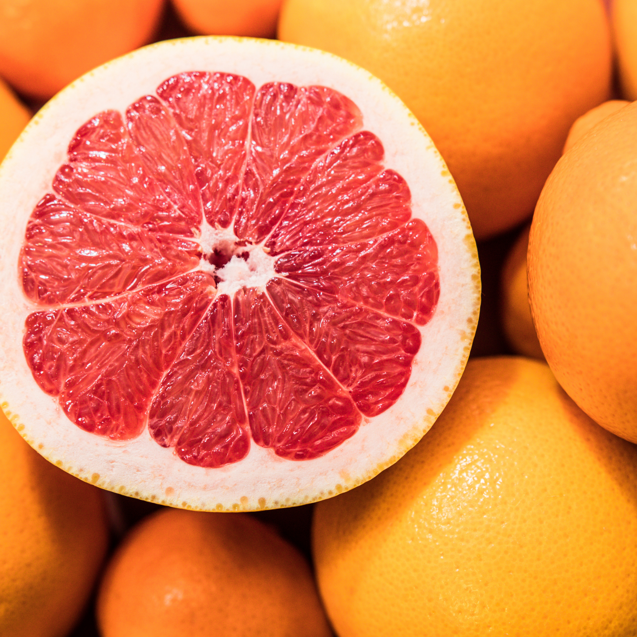 Close-up of a halved pink grapefruit surrounded by whole oranges.