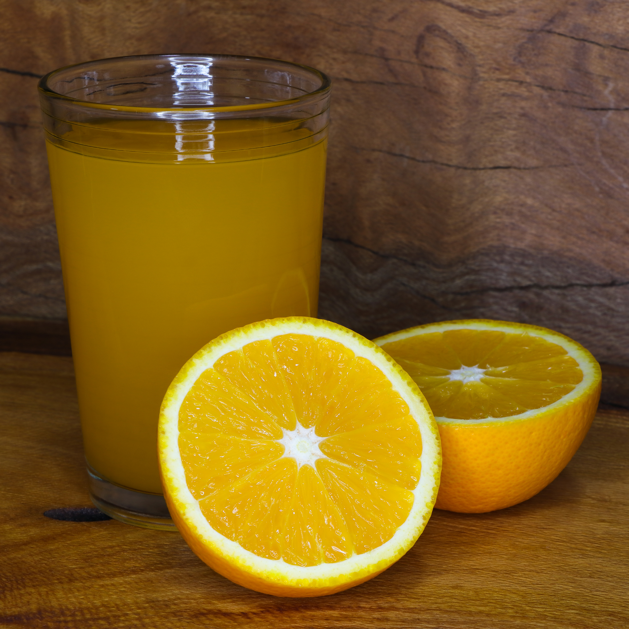 Glass of orange juice with a sliced orange on a wooden surface