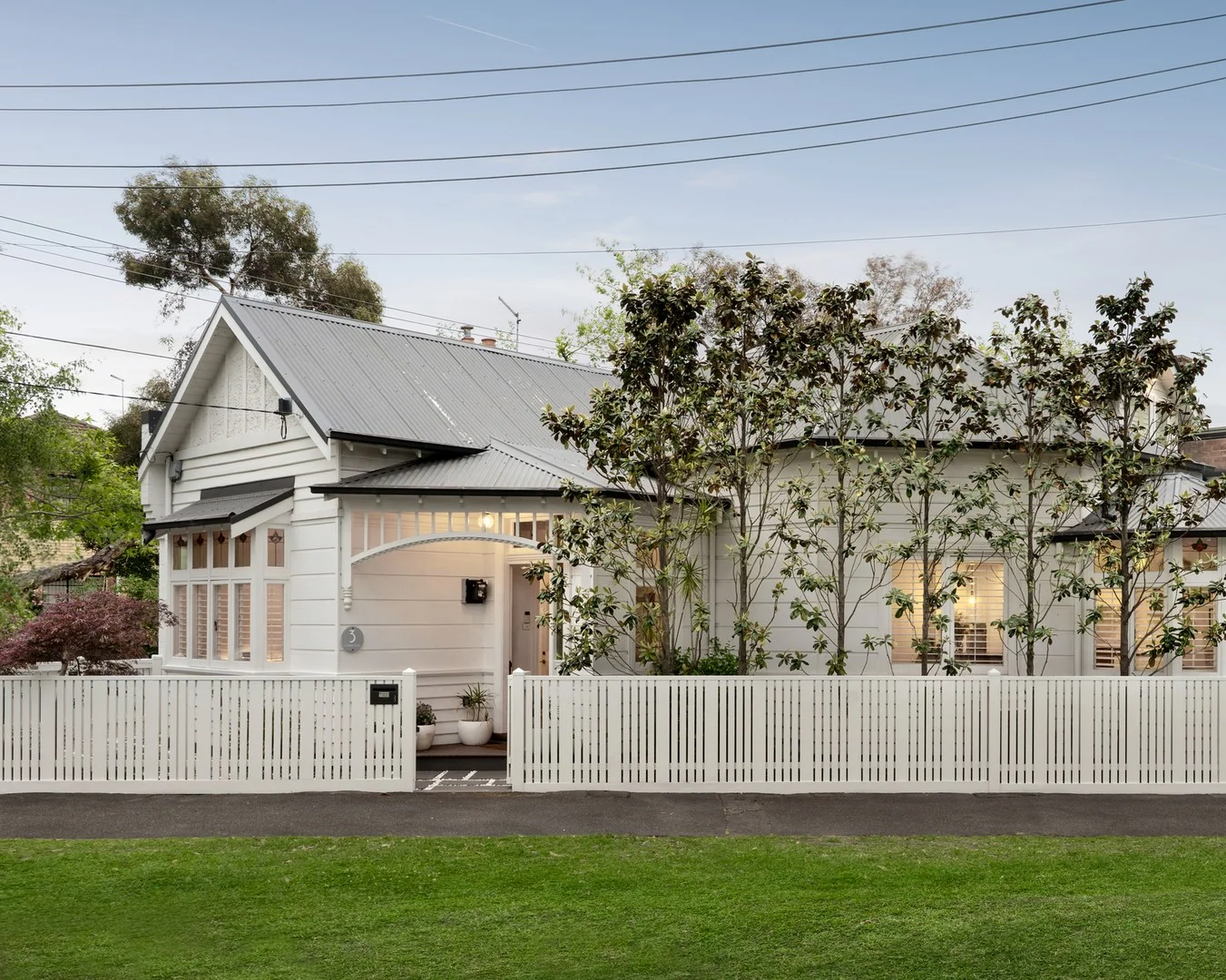 White house with a white picket fence and trees in front, under a clear blue sky.