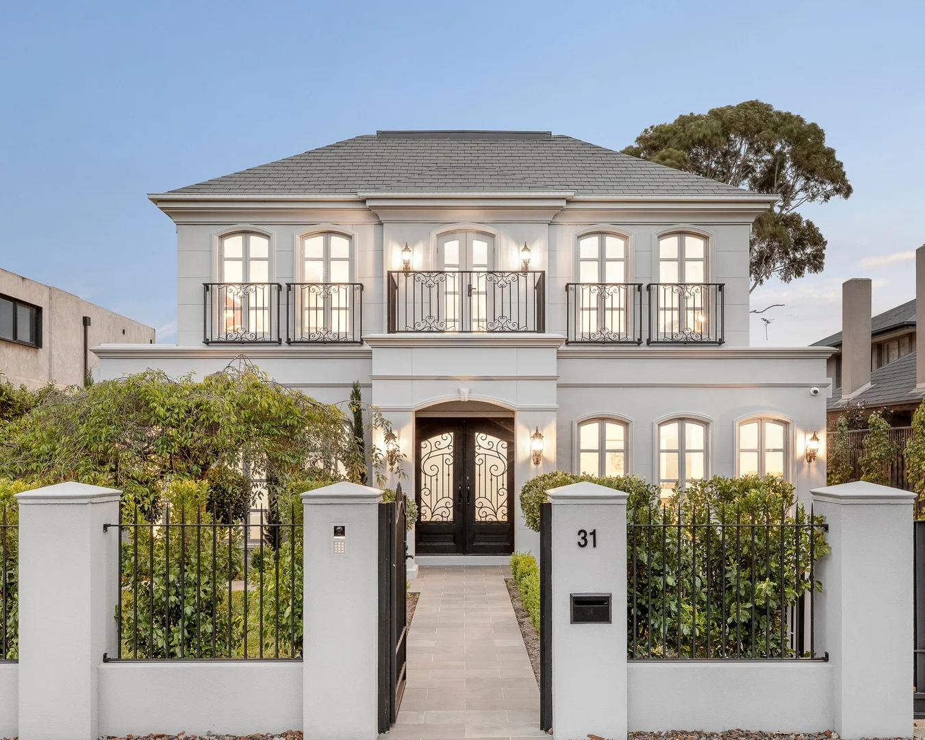 Stately two-story house with white facade and black accents, surrounded by greenery.