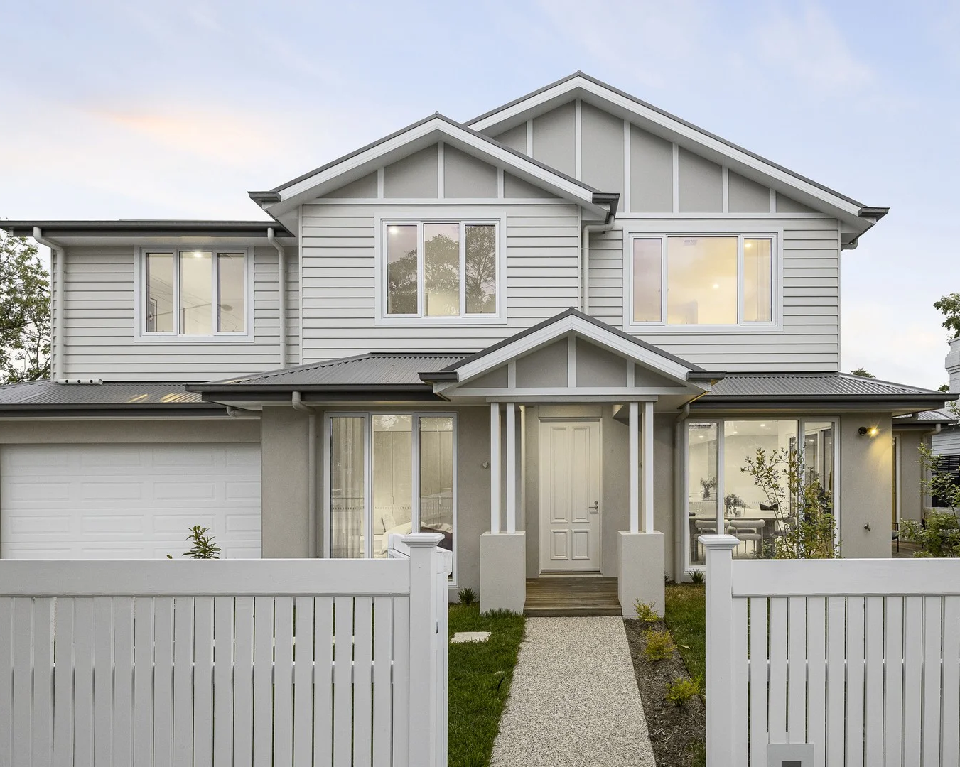 Two-story house with gray siding and white trim, surrounded by greenery.